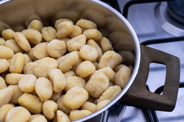 A pan of gnocchi simmering over a flame on a stovetop in a traditional restaurant kitchen, with golden pieces gently cooking in the rustic setting.