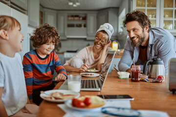 Happy family enjoying breakfast together in modern kitchen with laptop