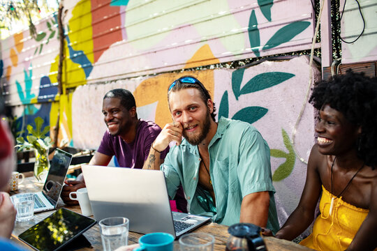 Happy friends working on laptops outdoors at hostel