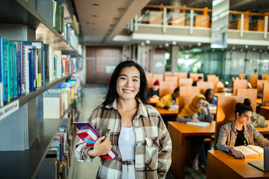 Portrait of a female student in library holding books and smiling