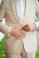 Groom Adjusting His Beige Wedding Suit: Close-up of a man's hands buttoning a stylish beige suit jacket, showcasing the details of his attire, perfect for wedding preparation or formal event imagery
