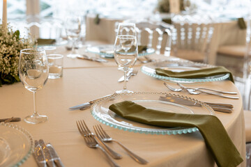 Elegant Table Setting for a Special Event: Detailed shot of a beautifully arranged table with glass chargers, olive green napkins, and wine glasses, perfect for upscale dining, weddings