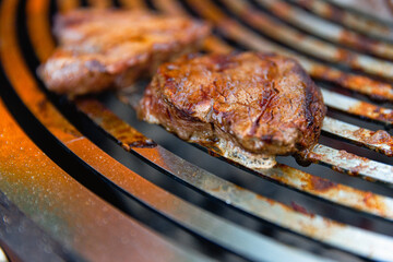 Juicy, seasoned meat steaks sizzle on a grill grate over burning coals, with flames and smoke rising as they cook to perfection.
