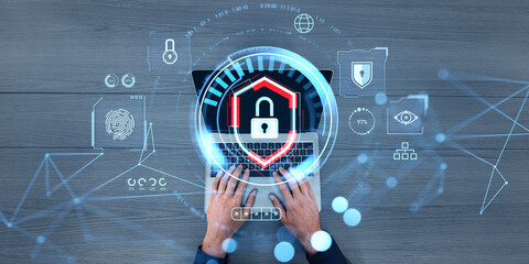 Hands typing on laptop with cybersecurity holograms on wooden background.