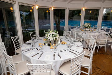 Elegant Round Table Setting at an Event: A beautifully prepared round table with white linens, chairs, cutlery, and a white floral centerpiece, perfect for a wedding reception, formal dinner