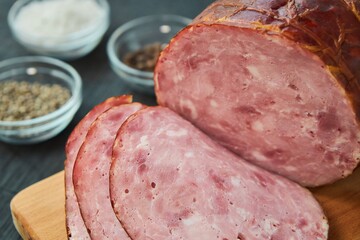 The ham lies on a wooden surface surrounded by spices. Meat production.