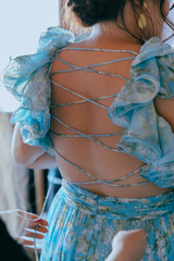 Female hands tying a bridesmaid's open-back blue dress at an elegant wedding.