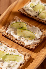 Wholegrain toast with tsasiki greek souce and cucumber on wooden plate in sunny atmosphere