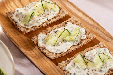 Wholegrain toast with tsasiki greek souce and cucumber on wooden plate in sunny atmosphere