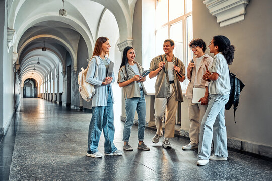 College students stand and talk in the university building. Multiethnic young people stand near classes, diverse college friends spending time indoors after lessons.