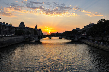 The Seine River in Paris with a historic bridge and the illuminated Eiffel Tower in the background. The calm water reflects the city lights, creating a romantic atmosphere of a Parisian evening