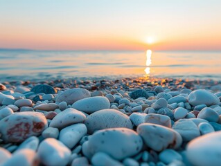 Smooth white pebbles on a beach with the sun rising over the horizon.