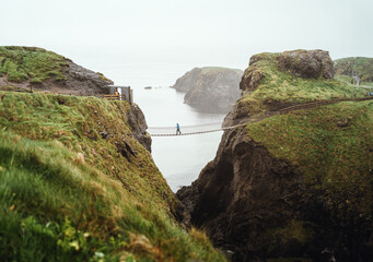 Frau in blauer Regenjacke an der Carrick-A-Rede Hängebrücke Wanderweg an Carrick Island Insel in...