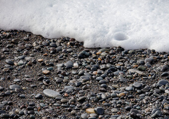 Wave of sea foam hitting pebbles on the beach