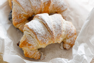 Croissant sprinkled with powdered sugar on a white pergamin paper, close-up. 
