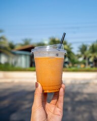 A Hand Holding an Iced Coffee in Front of a Bright Outdoor Setting, Symbolizing Refreshment and Energy.