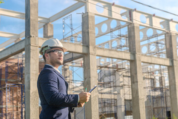 Asian adult foreman stands in front of the construction inspecting a construction project with...