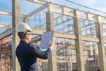 Asian adult foreman stands in front of the construction inspecting a construction project with...