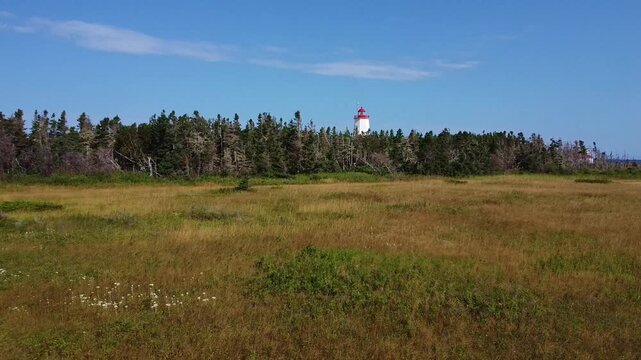 Drone s'approchant de la for&ecirc;t bordant le Phare Micsou , Birch Point, Nouveau-Brunswick. Survol de la for&ecirc;t de conif&egrave;res sous un ciel bleu parsem&eacute; de nuages vers le Phare de l'Ile Miscou. 