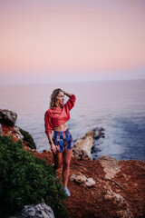 Young woman standing on a cliff by the ocean at sunset in a coastal location