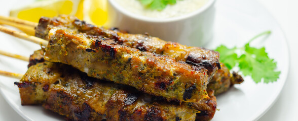 A plate of few skewers of meat with a side of sauce