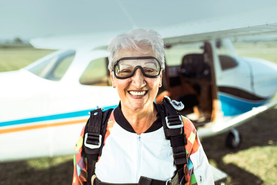 Portrait of a smiling elderly woman in skydiving gear standing in front of plane