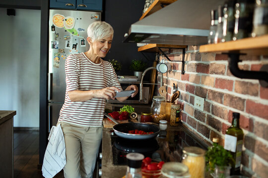 Smiling senior woman taking pictures of healthy meal in her modern kitchen
