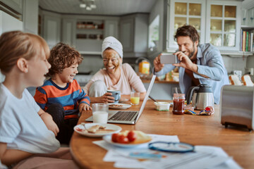 Happy family enjoying breakfast together in modern kitchen with laptop
