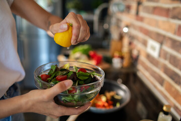 Close up of woman squeezing lemon on fresh salad in a kitchen setting