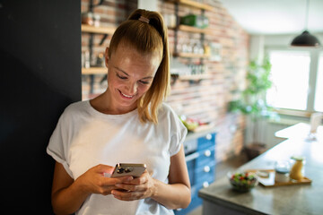 Smiling young woman using smartphone in modern kitchen