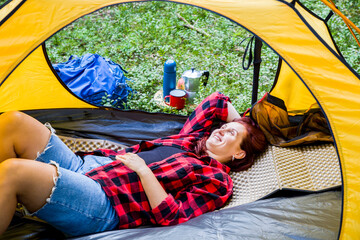 Camping on a clearing in the middle of the forest. A young girl is resting in a tent.