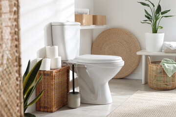 White toilet bowl, paper rolls and houseplants in bathroom