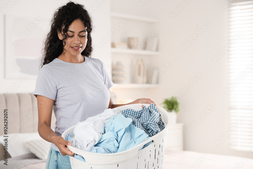 Wall mural Happy woman with basket full of laundry in bedroom, space for text