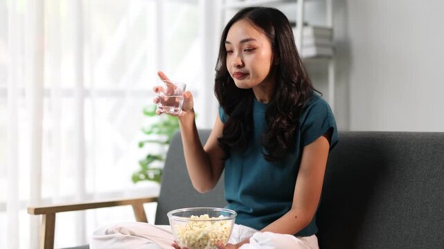 Young woman at home eating snacks and drinking water. A woman eats popcorn stuck in her throat and she drinks water.