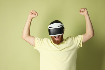 Emotional man using virtual reality headset on pale green background
