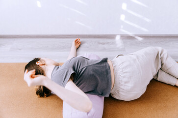 Woman in casual clothing practicing yin yoga pose reclined twist on bolster