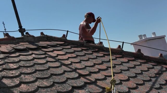 The roof worker maintains the roof. Roof worker with safety rope and roofing harness safety kit. Roof worker adjusts his safety harness. Concept of work safety when working at heights