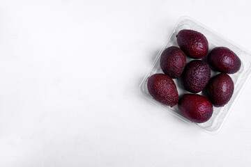 Purple avocados in the plastic box on white background. Mockup with copy space