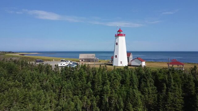 Drone frolant la coupole au sommet du Phare Micsou , Birch Point, Nouveau-Brunswick. Survol de la for&ecirc;t de conif&egrave;res sous un ciel bleu parsem&eacute; de nuages vers le Phare de l'Ile Miscou.