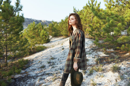 Woman in plaid shirt and boots standing proudly on hill overlooking dense forest