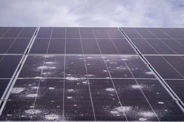 Close-up of solar panel damage caused by hailstorm, showcasing cracked and dented photovoltaic cells under cloudy skies, emphasizing the impact of extreme weather on renewable energy systems.