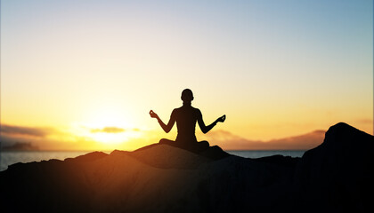 Woman meditating at sunset on a mountain, silhouetted against a serene sky.