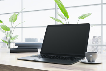 Fototapeta premium Modern laptop on desk with cup of coffee in bright office with large windows. 3D Rendering