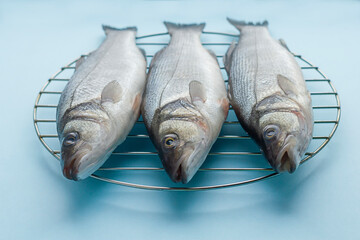 Fresh raw sea bass fish on the grill on a blue background. Proper nutrition, Mediterranean diet.