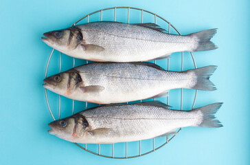 Three fresh sea bass on the grill on a blue background. Natural sea fish, healthy nutrition, Mediterranean diet.