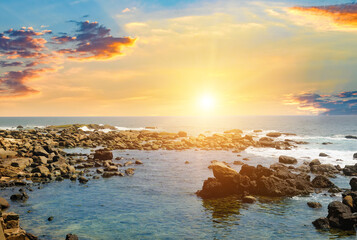 Seascape with beautiful waves, rocky shore and bright sunrise .