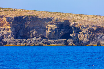 Coastal cave and jagged rocks at seaside. Rocky cliff overlooks Mediterranean Sea in Malta