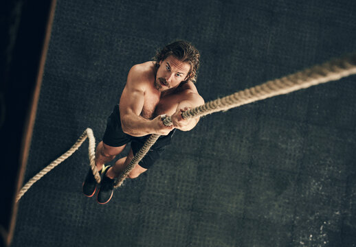 Body, exercise and rope climbing with man in gym from above for challenge, performance or workout. Fitness, target and wellness with serious climber in health club for physical or strength training