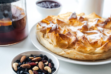Homemade pastries, apple pie made of filet dough, nuts and tea on a white table. Selected focus. High quality photo