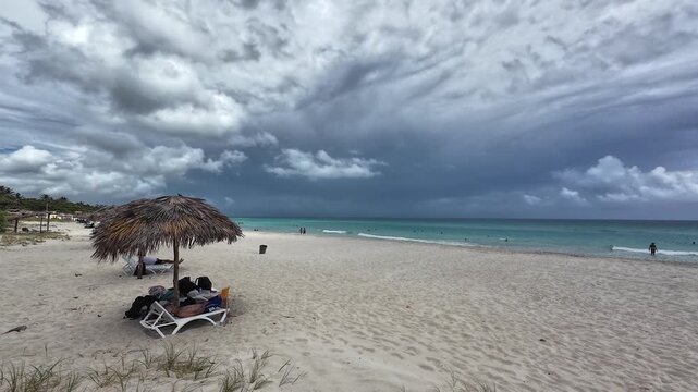 Straw beach umbrella with beach-chair under a partly cloudy sky on a sandy beach in Varadero, Cuba